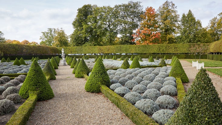 The garden in October at Ham House and Garden, Surrey, with triangular beds filled with ball-shaped topiary shrubs, with cone-shaped topiary trees at each corner
